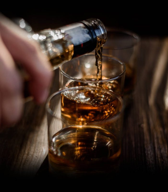 Pouring strong alcohol drink into the glasses which are on the wooden table